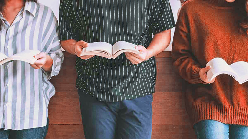 Three teens standing against a wall, with books open in front of them