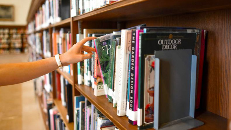 Hand pulling a book from a library shelf.